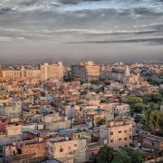 Wide view of a Tier-2 Indian city with dense low-rise housing, mid-rise commercial buildings, and a growing urban skyline under a cloudy sky.