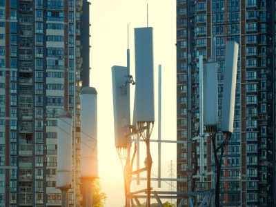 5G cellular antennas mounted on a telecom tower between high-rise residential buildings at sunset, representing urban digital infrastructure and connectivity.