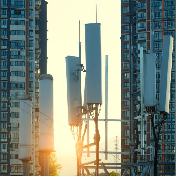 5G cellular antennas mounted on a telecom tower between high-rise residential buildings at sunset, representing urban digital infrastructure and connectivity.