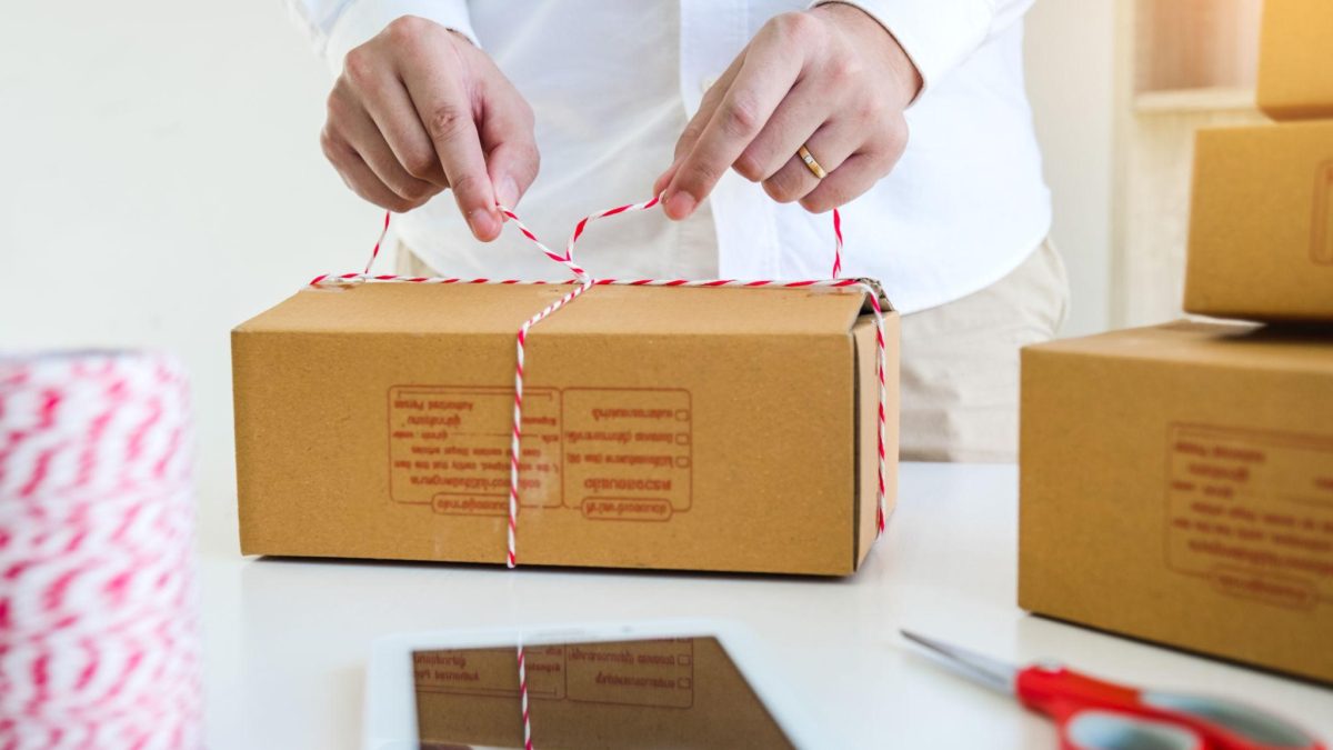 Person tying a cardboard box with string on a table, packaging an order for an e-commerce or D2C business.
