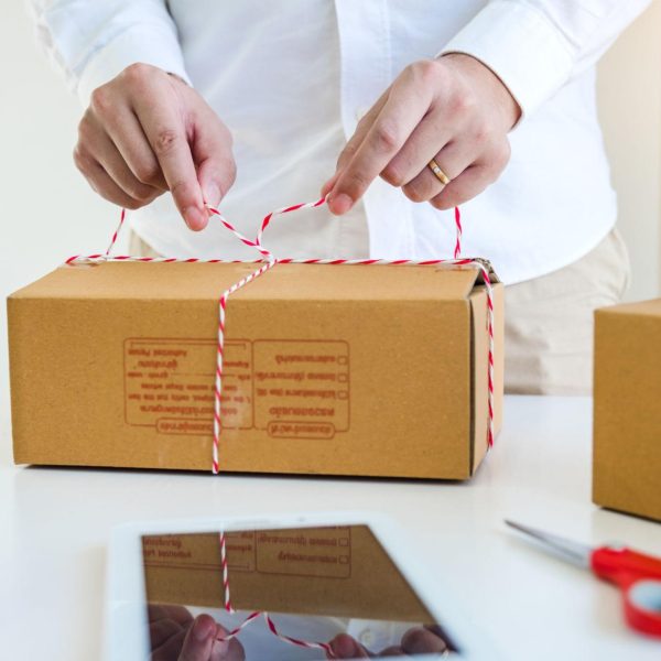 Person tying a cardboard box with string on a table, packaging an order for an e-commerce or D2C business.