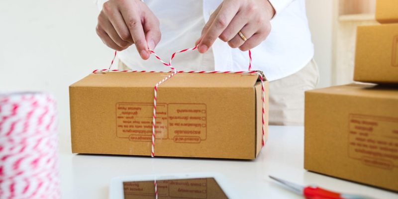 Person tying a cardboard box with string on a table, packaging an order for an e-commerce or D2C business.