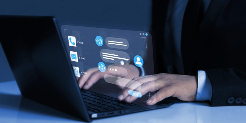 Person using a laptop with a virtual chatbot interface displayed on screen, showing automated customer support and digital communication icons.