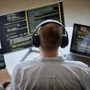 Developer wearing headphones working on multiple screens displaying code on a laptop and monitors in a modern workspace.