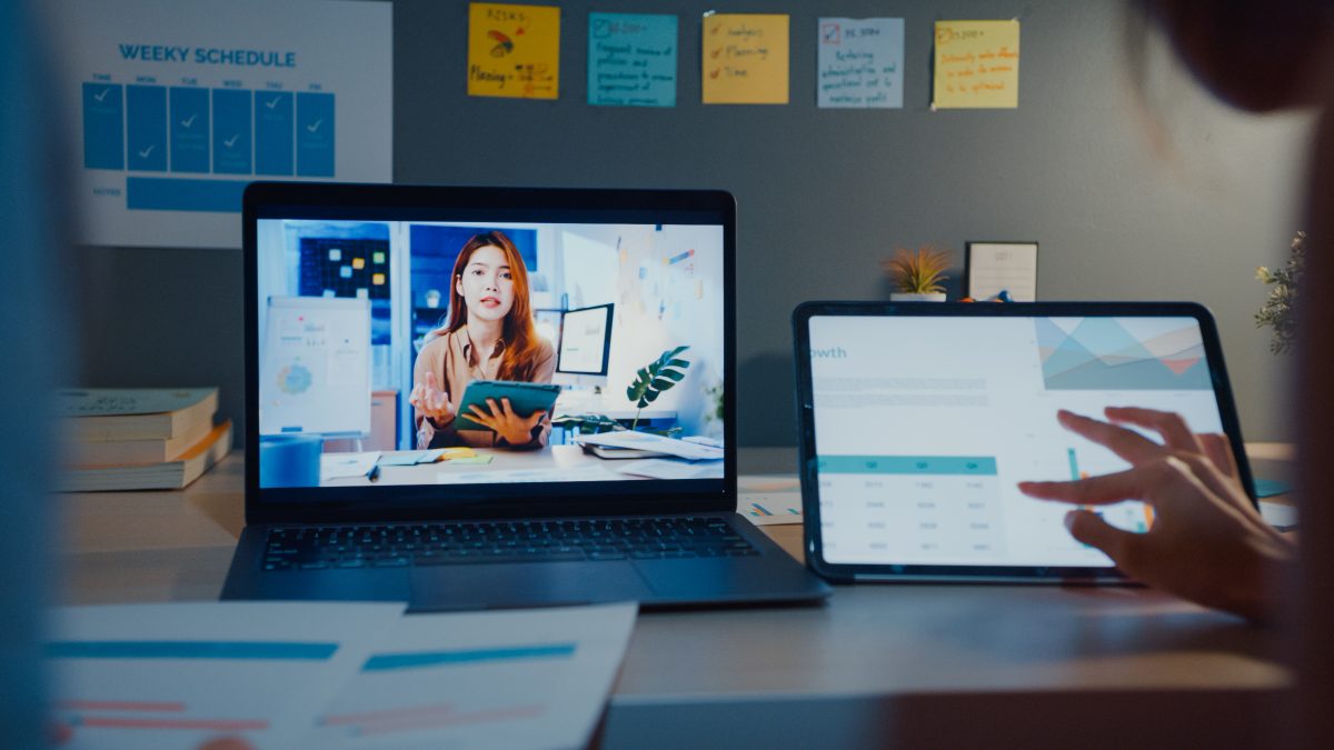 Student attending an online class on a laptop and tablet at home at night.