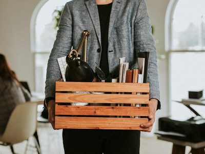 Employee holding a box of office belongings after a corporate layoff in a modern workplace environment.