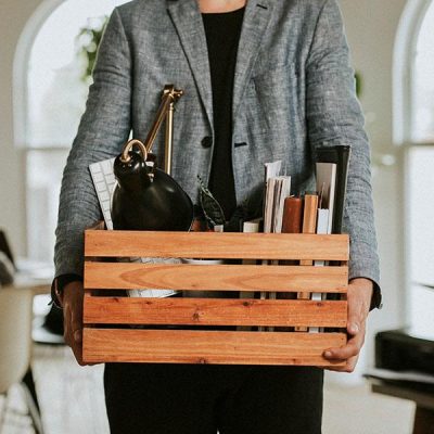 Employee holding a box of office belongings after a corporate layoff in a modern workplace environment.