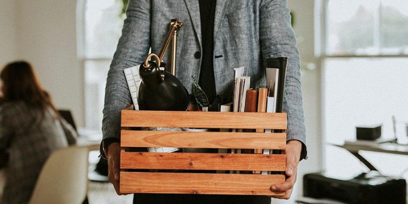 Employee holding a box of office belongings after a corporate layoff in a modern workplace environment.