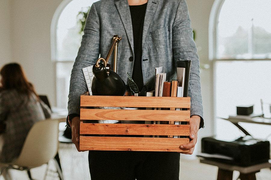 Employee holding a box of office belongings after a corporate layoff in a modern workplace environment.