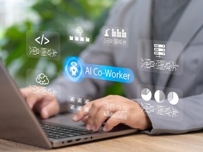 Professional using a laptop with a digital AI co-worker interface displayed on screen, featuring data analytics, cloud storage, coding, and workflow automation icons representing AI-powered workplace productivity and collaboration.