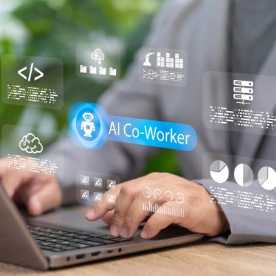 Professional using a laptop with a digital AI co-worker interface displayed on screen, featuring data analytics, cloud storage, coding, and workflow automation icons representing AI-powered workplace productivity and collaboration.