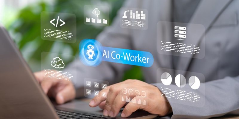 Professional using a laptop with a digital AI co-worker interface displayed on screen, featuring data analytics, cloud storage, coding, and workflow automation icons representing AI-powered workplace productivity and collaboration.